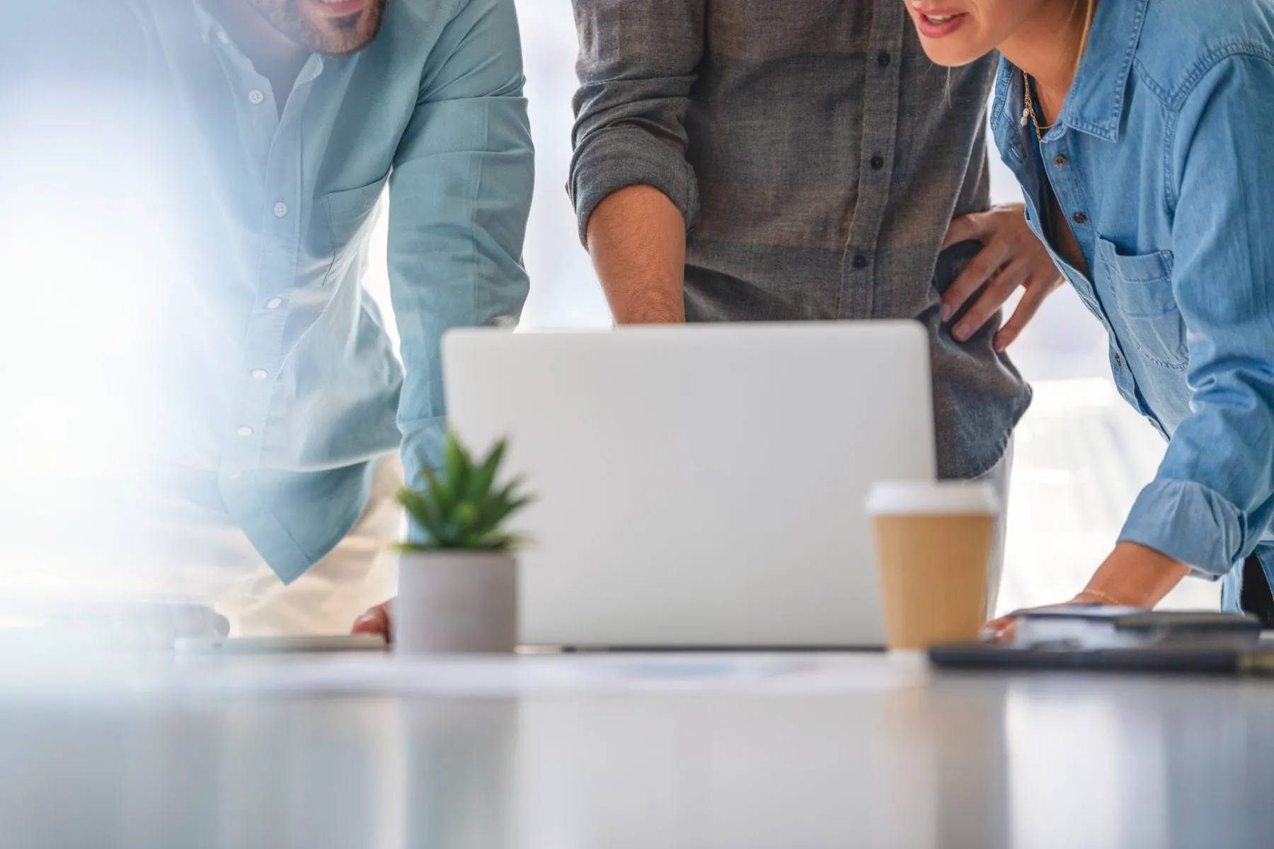 Three people look at a laptop together on a work table.