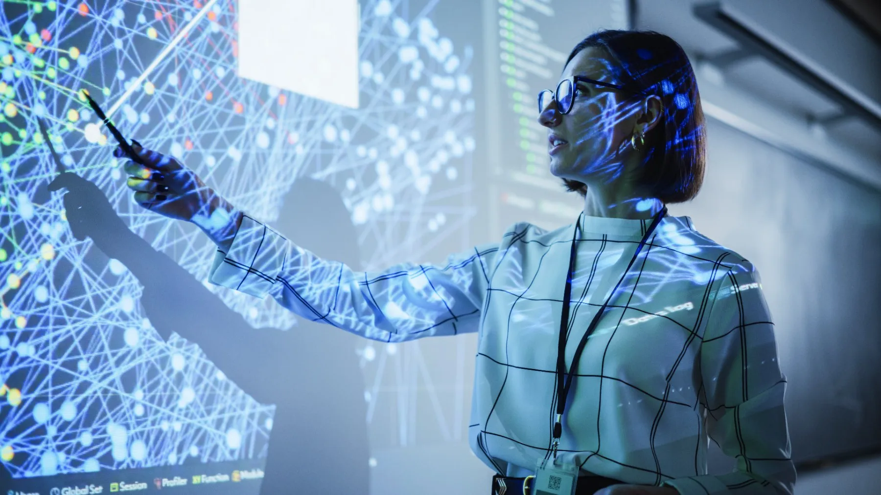 A woman in glasses uses a pointer to indicate a network graph projected on a large screen.
