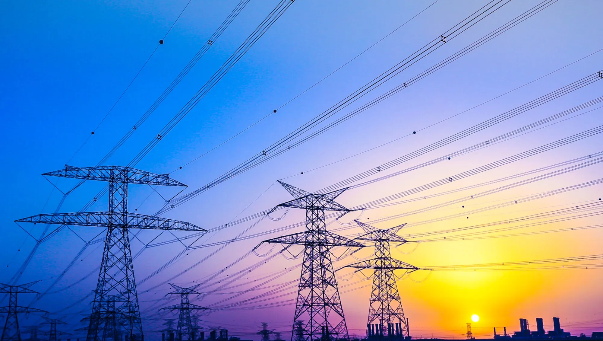 High-voltage pylons and power lines silhouetted against a sunset sky.