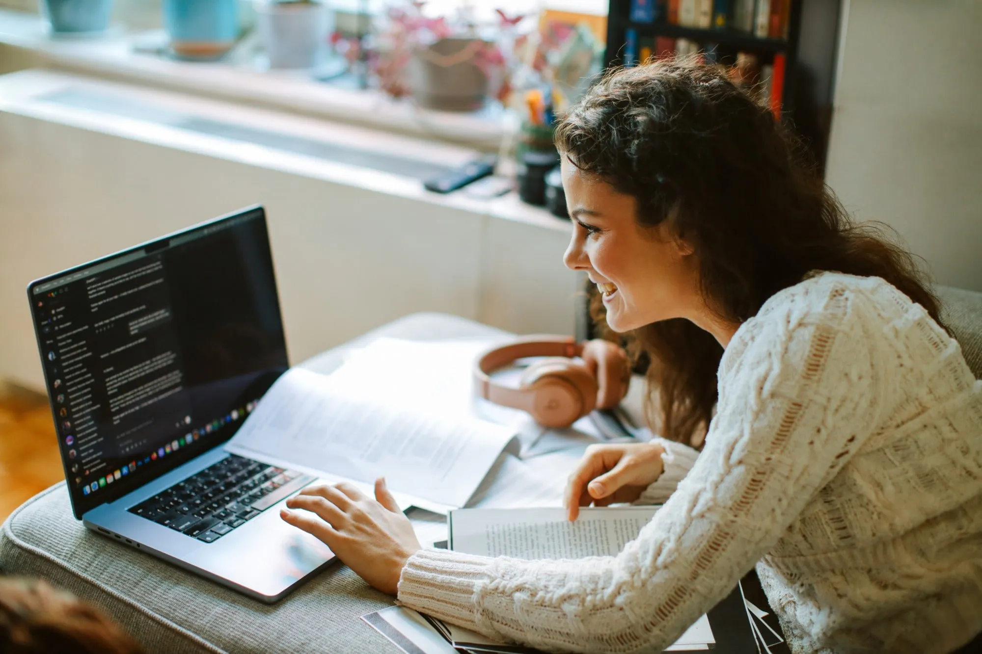 A student smiles as she uses a laptop, with open books and notes on the table.