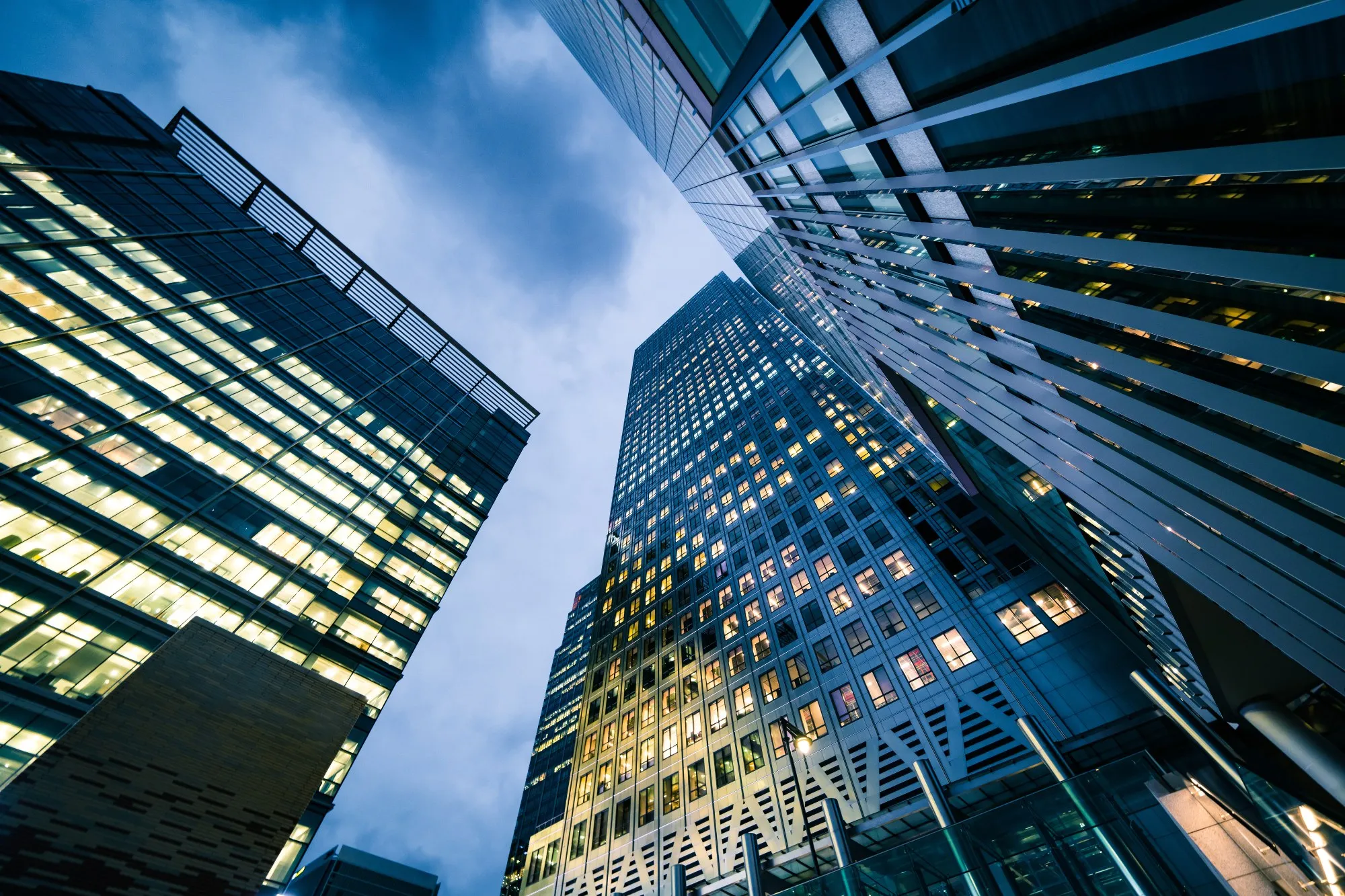 Office skyscrapers with lit windows, seen from below at dusk.