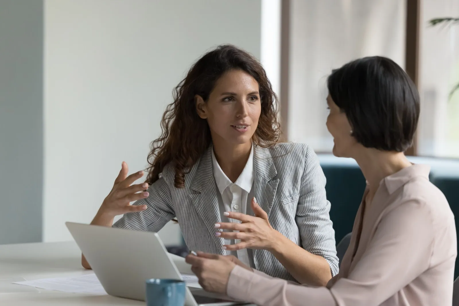 Dos profesionales conversan junto a un portátil en una mesa de trabajo.