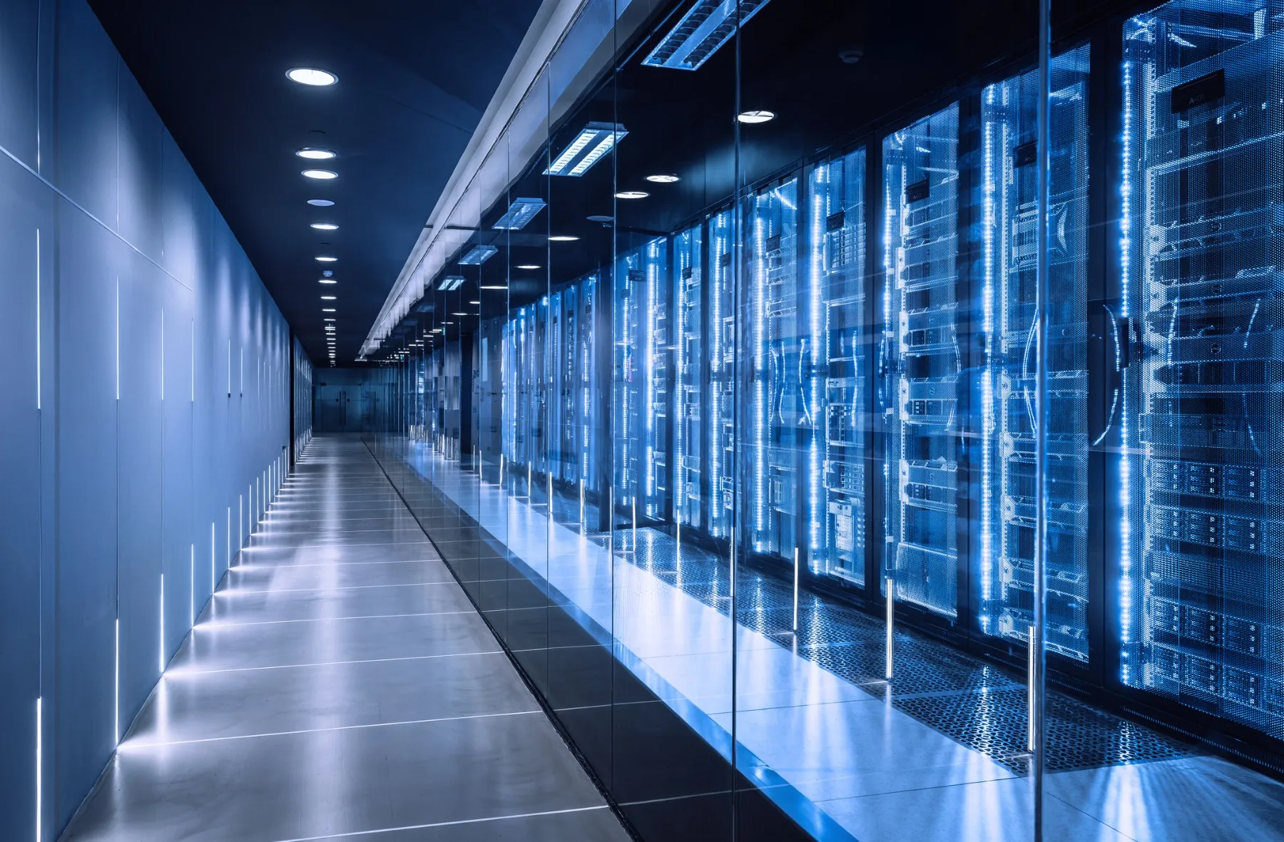 A data centre aisle with server cabinets lit up behind glass panels.